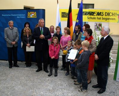 Innenminister Herrmann, flankiert von Wolfgang Prestele (ganz rechts) und Günter Fuchs von der Landesverkehrswacht (ganz links), zeichnen das vorbildhafte ehrenamtliche Engagement von Schulweghelfern aus dem Landkreis Neuburg/Donau in Gegenwart von Schulkindern aus